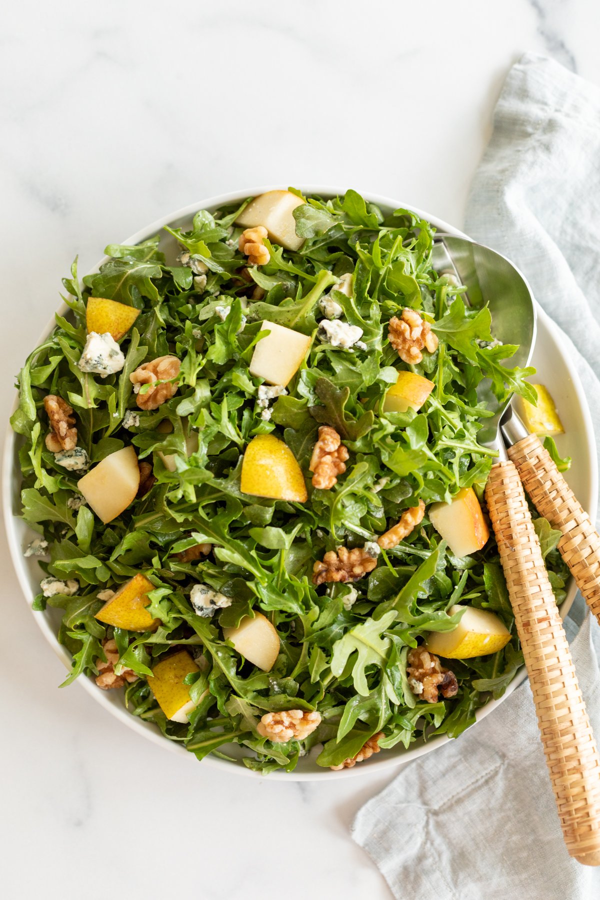 A white bowl full of pear salad, with arugula, walnuts and gorgonzola.