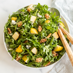 A white bowl full of pear salad, with arugula, walnuts and gorgonzola.