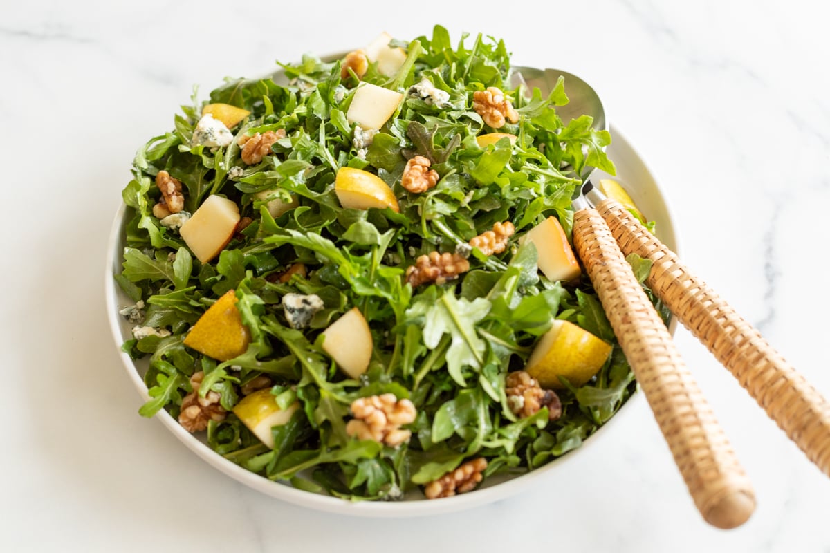 A white bowl full of pear salad, with arugula, walnuts and gorgonzola.