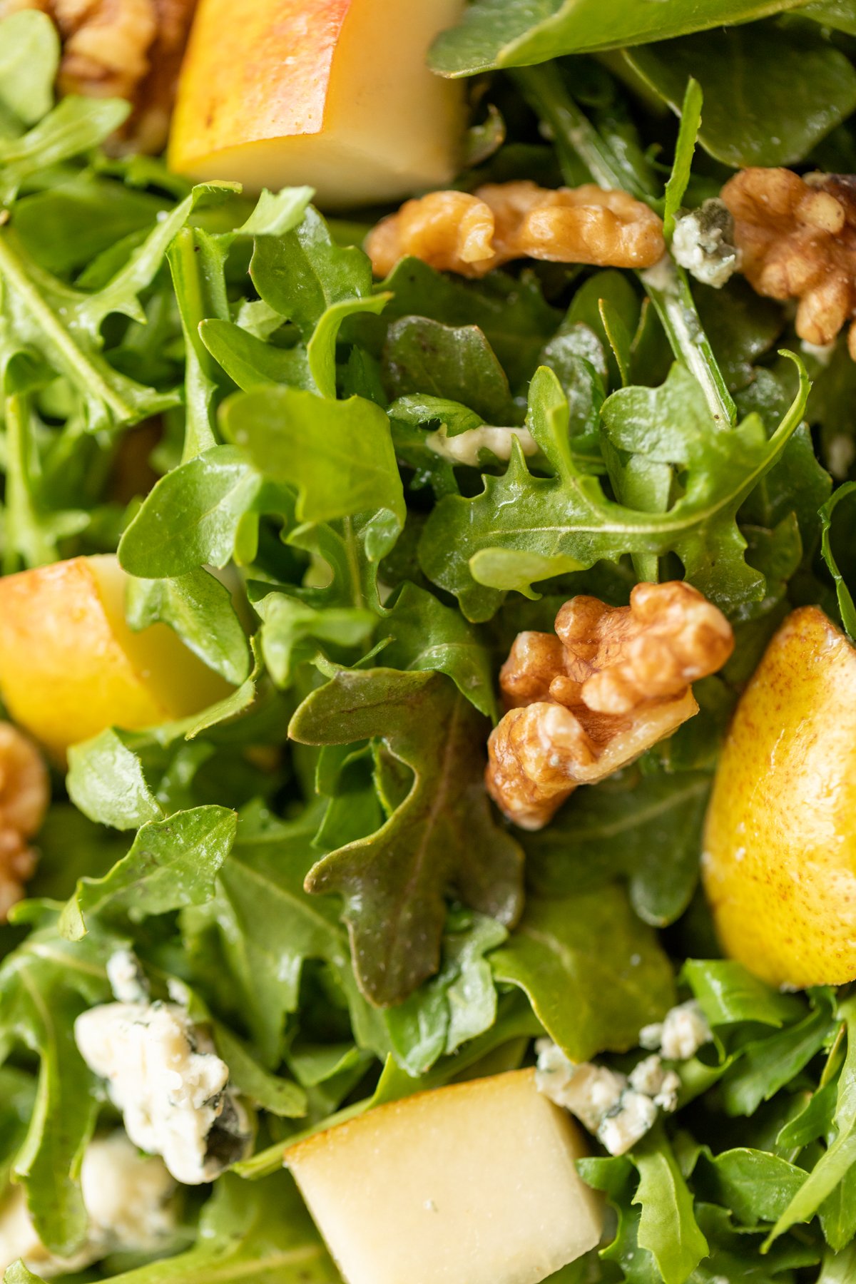 A white bowl full of pear salad, with arugula, walnuts and gorgonzola.