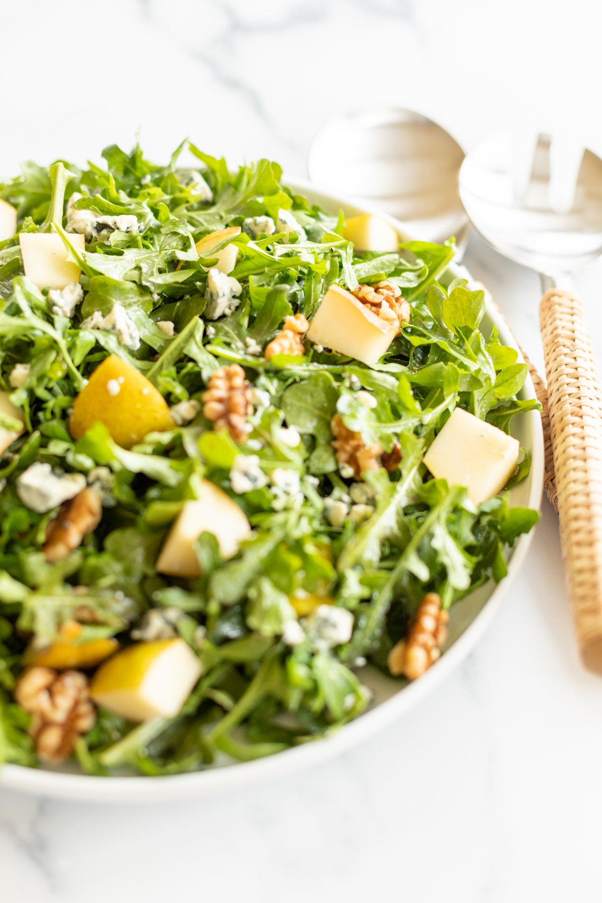 A white bowl full of pear salad, with arugula, walnuts and gorgonzola.