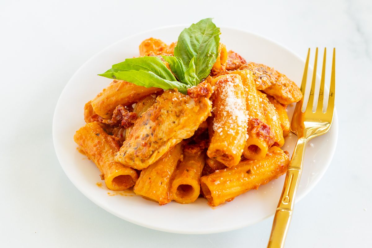 Sun dried tomato chicken pasta on a white plate with a gold fork to the side.