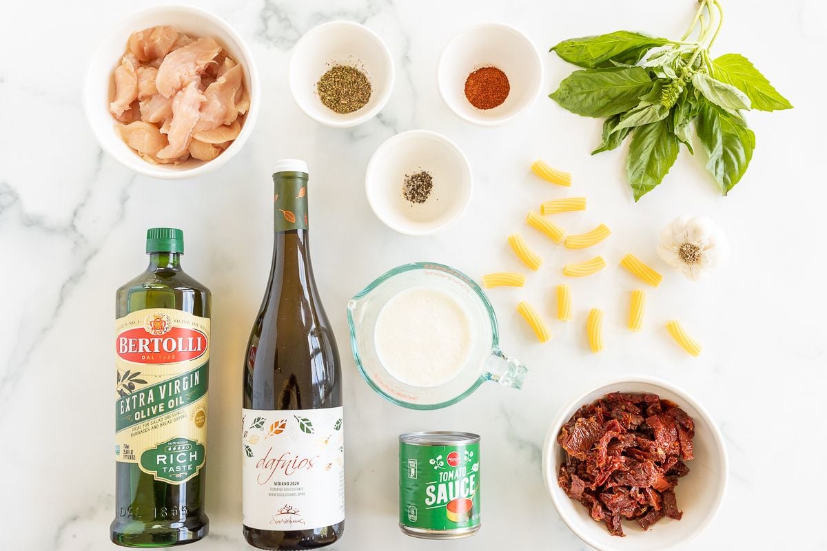 Ingredients for sun dried tomato chicken pasta on a marble countertop.