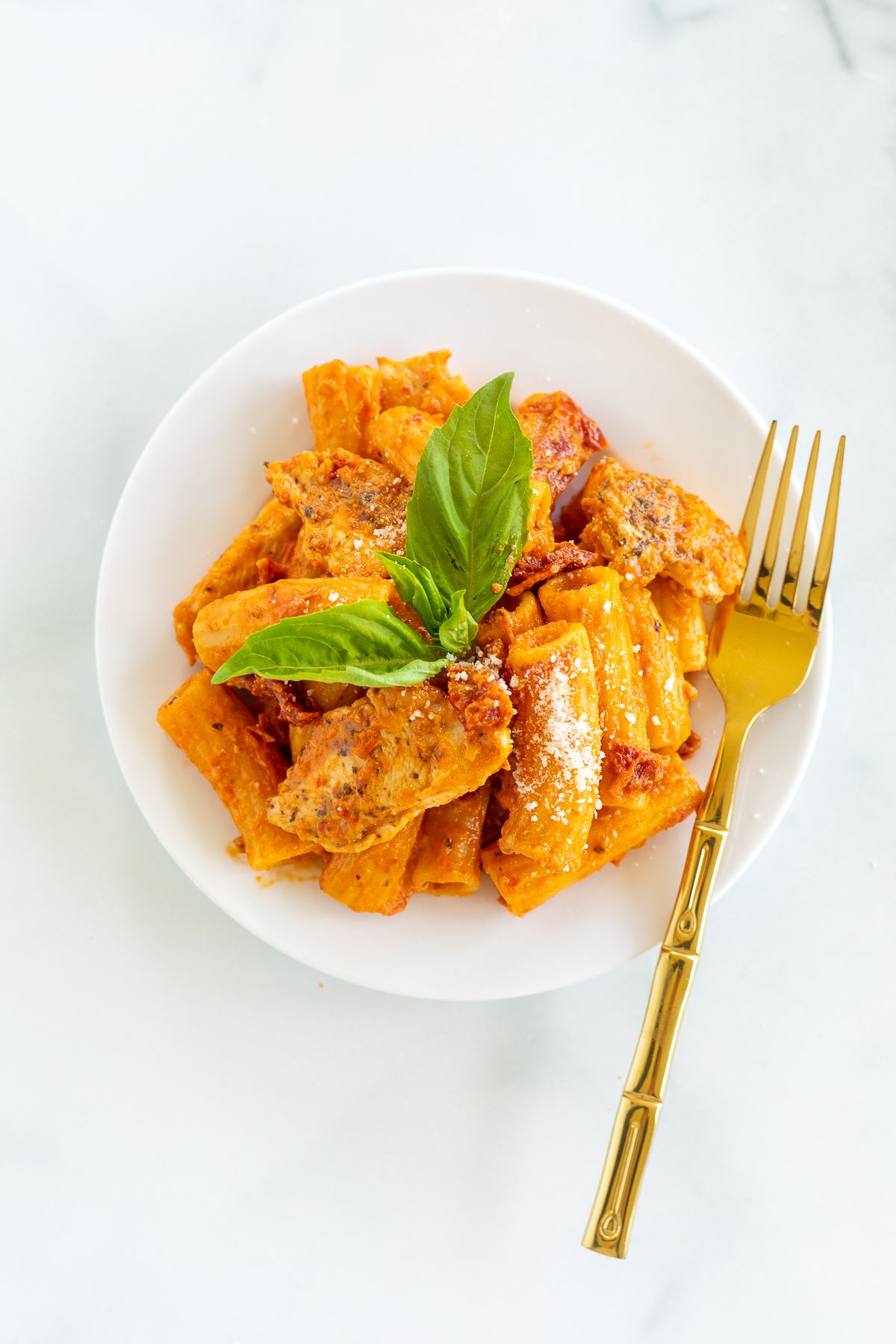 Sun dried tomato chicken pasta on a white plate with a gold fork to the side. 