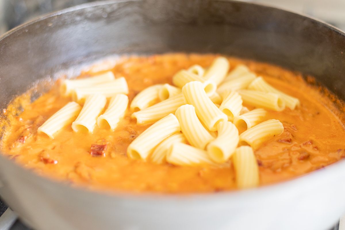 Sun dried tomato chicken pasta sauce in a pan with rigatoni on stovetop.