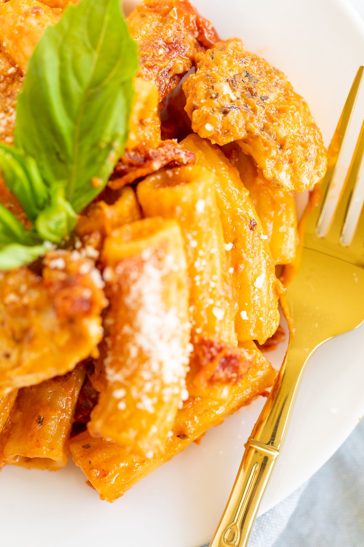 Sun dried tomato chicken pasta on a white plate with a gold fork to the side.