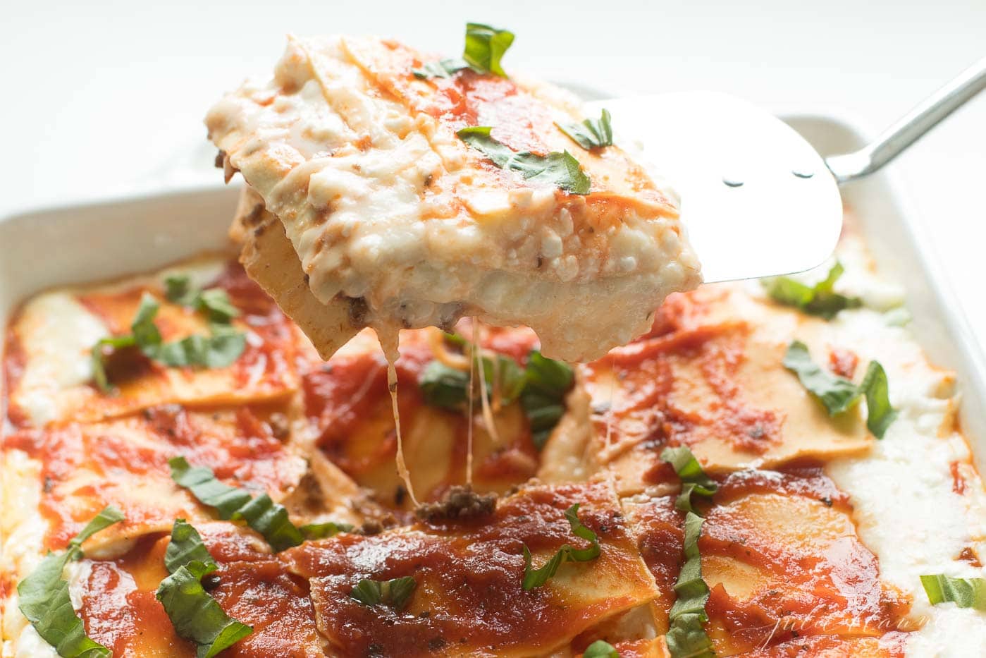 A lasagna with cottage cheese in a white pan, a slice being scooped out with a spatula.