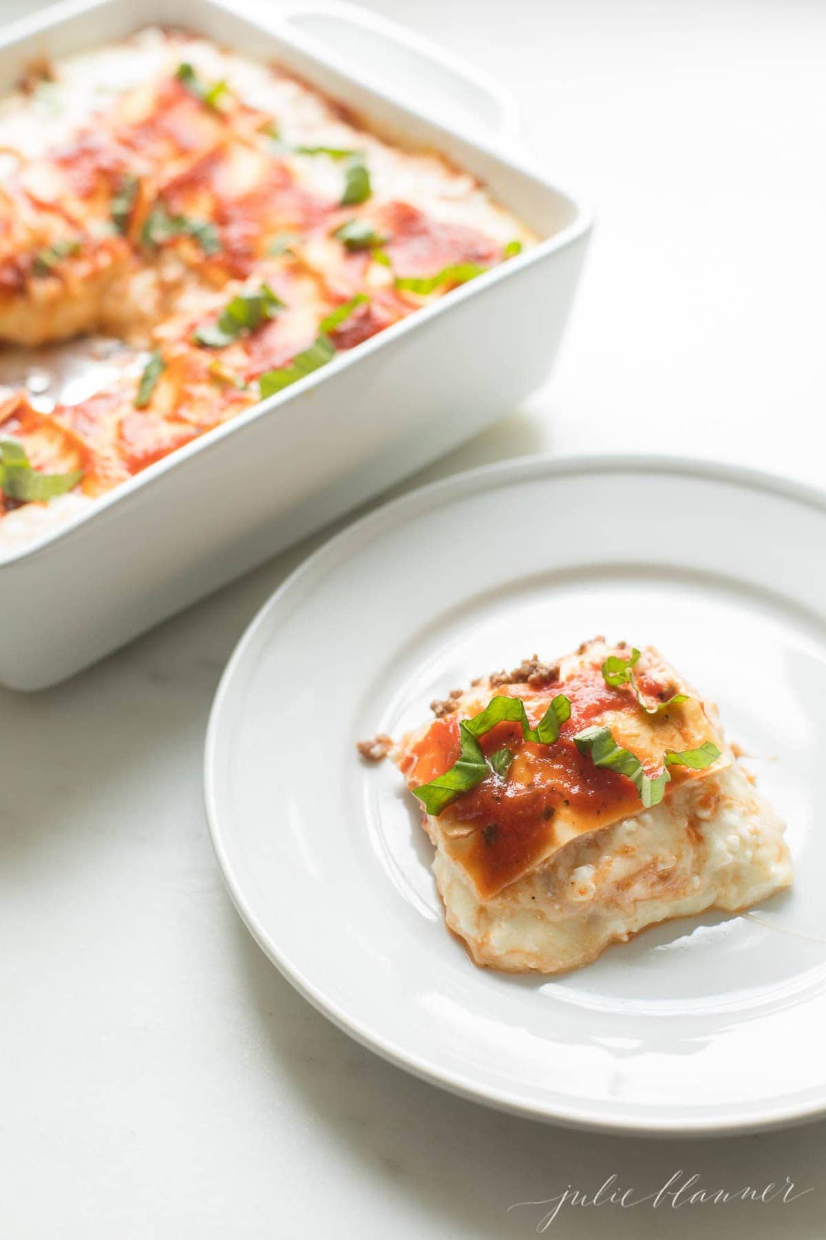 lasagna on white plate next to casserole dish