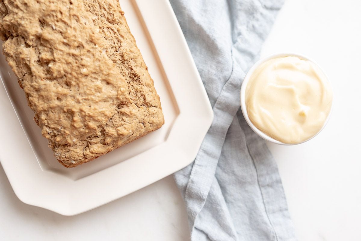 A loaf of beer bread on a white platter, with a small container of honey butter to the side