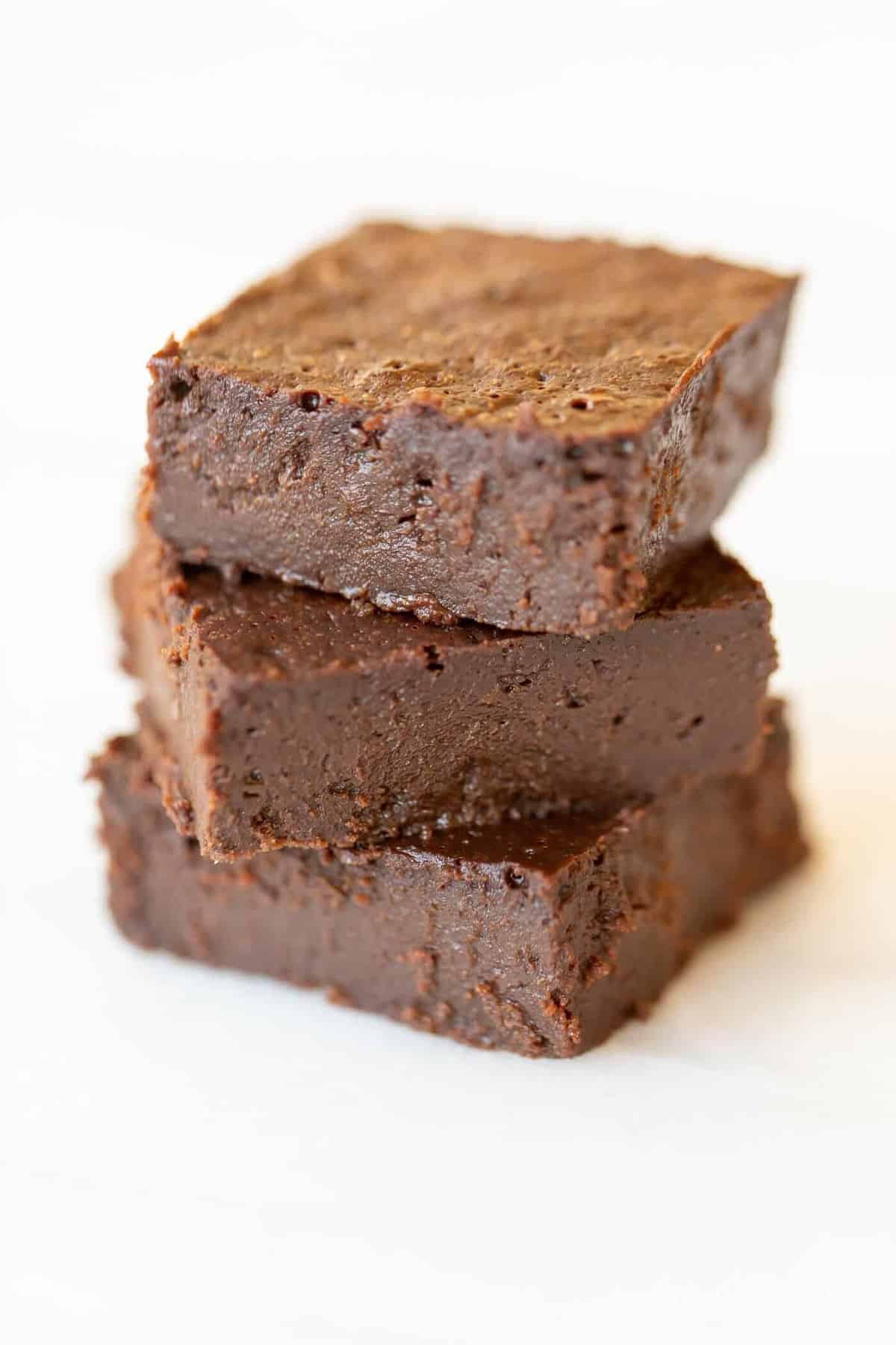 White surface with a stack of three dark chocolate brownies.