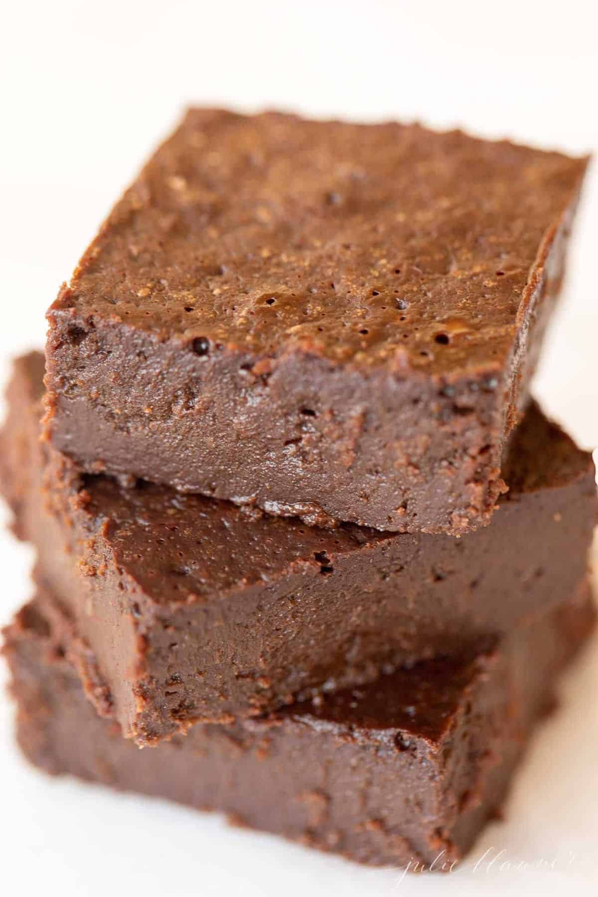 White surface with a stack of three no flour brownies.