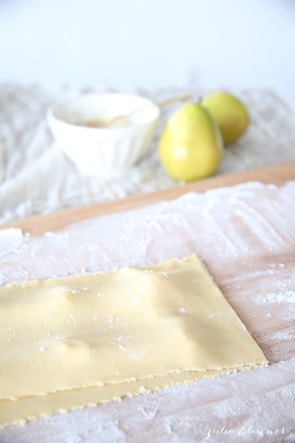 Two thin sheets of pasta on a floured wooden surface. 