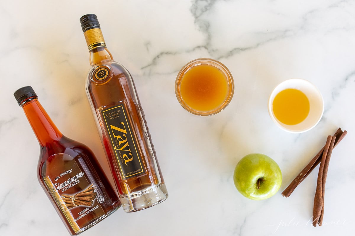 Ingredients for apple cider cocktails laid out on a marble countertop.