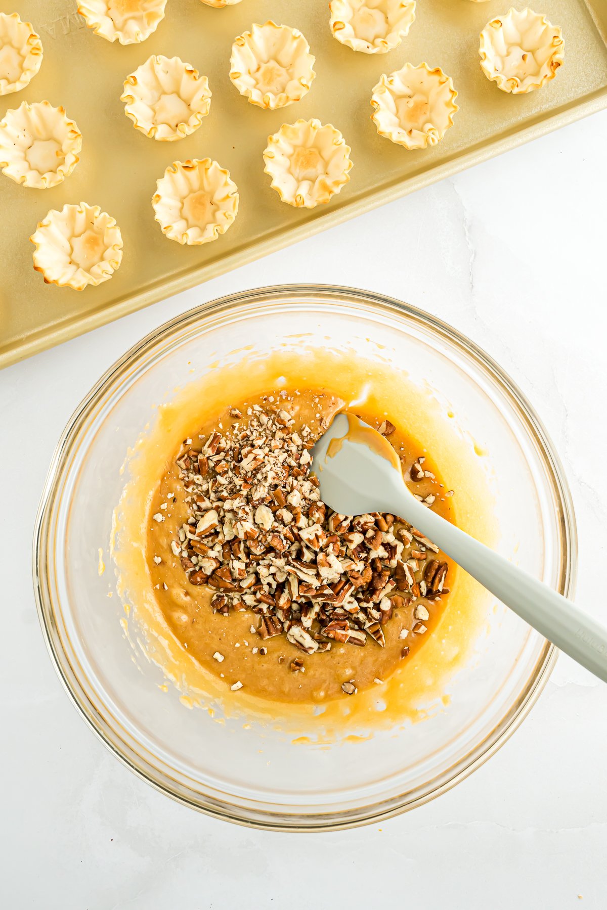 A glass bowl with a spoon in it, holding Mini Pecan Pie bites.