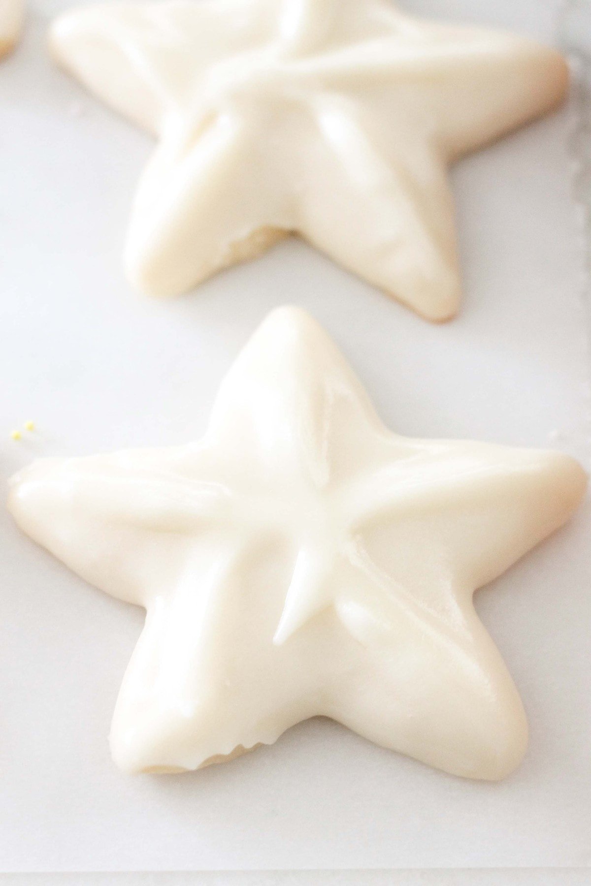 Two white sugar cookies topped with sugar cookie frosting recipe on parchment