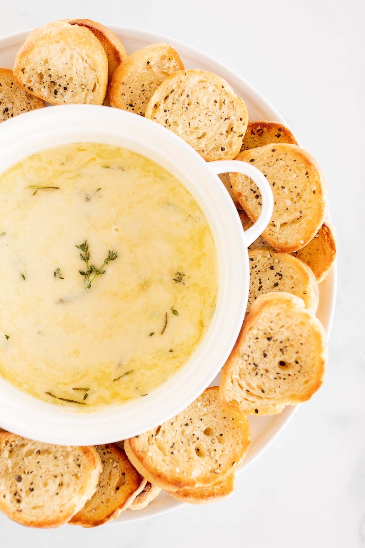 A white bowl of baked fontina cheese dip surrounded by crostini