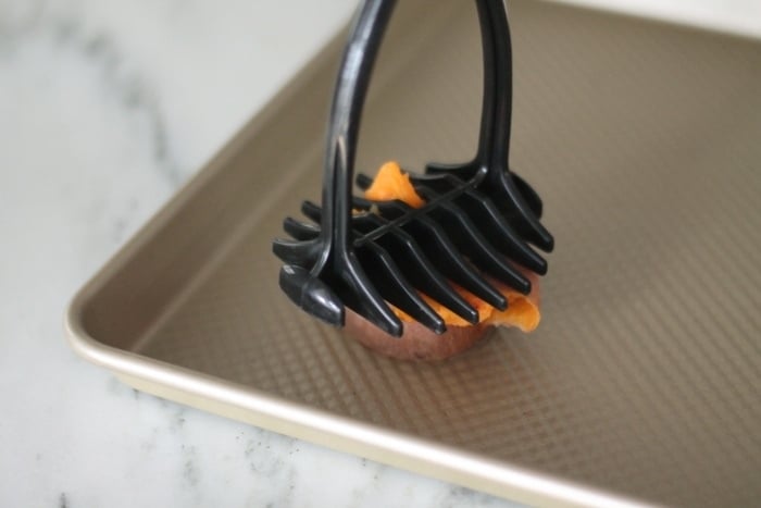 potato mashing smashing sweet potato on baking sheet