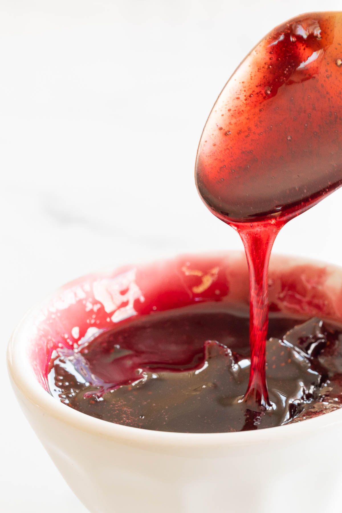 A spoon pulling strawberry sauce out of a small white bowl