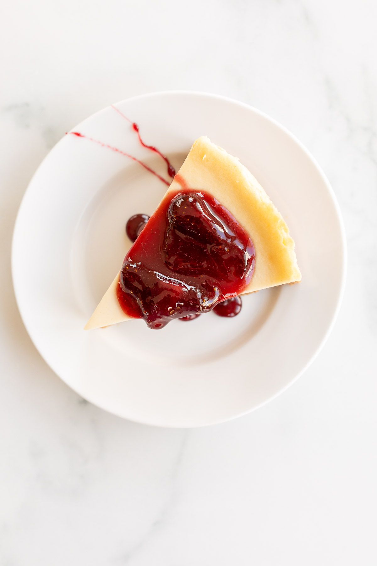 A white plate with a slice of cheesecake covered in strawberry topping for cheesecake