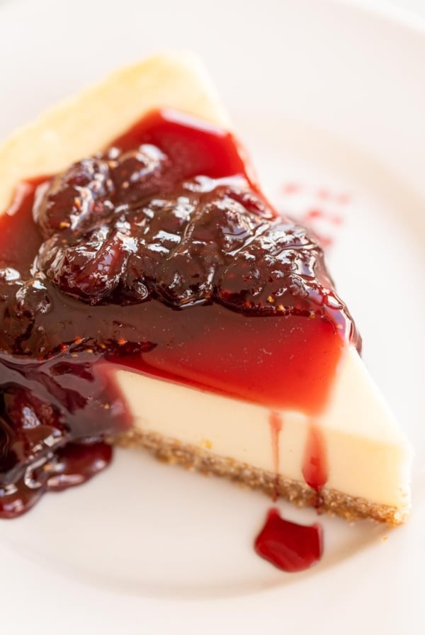 Strawberry topping for cheesecake on top of a slice of cheesecake on a white plate