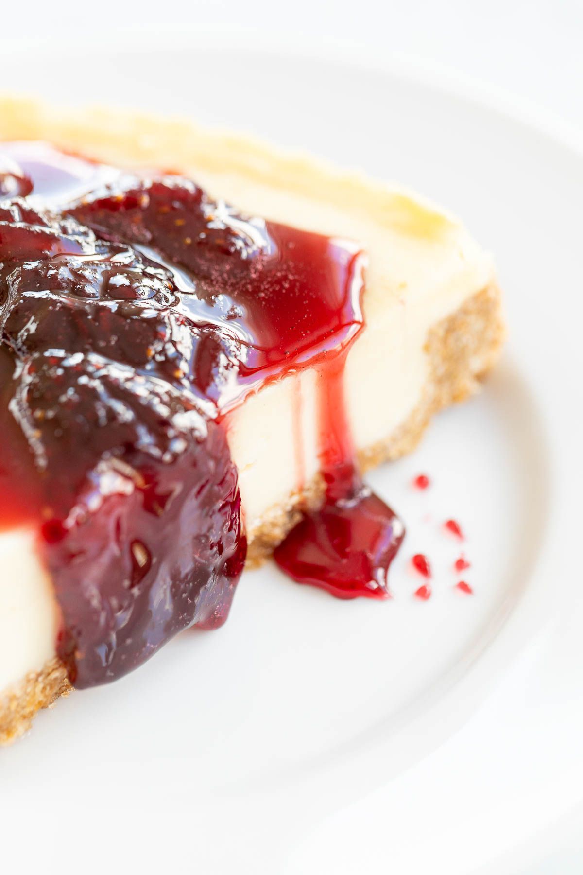 Strawberry topping for cheesecake on top of a slice of cheesecake on a white plate