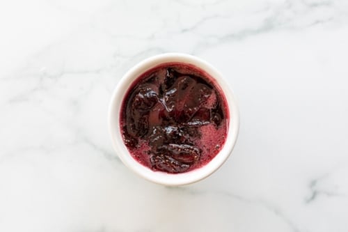 A white bowl full of strawberry sauce on a marble surface