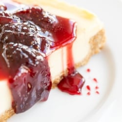 A white plate with a slice of cheesecake covered in strawberry topping for cheesecake