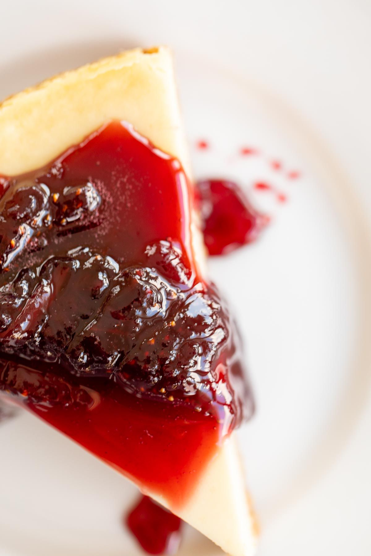 A white plate with a slice of cheesecake covered in strawberry topping for cheesecake