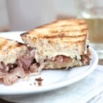 A grilled cheese, sliced on a white plate, with grill marks on the bread.