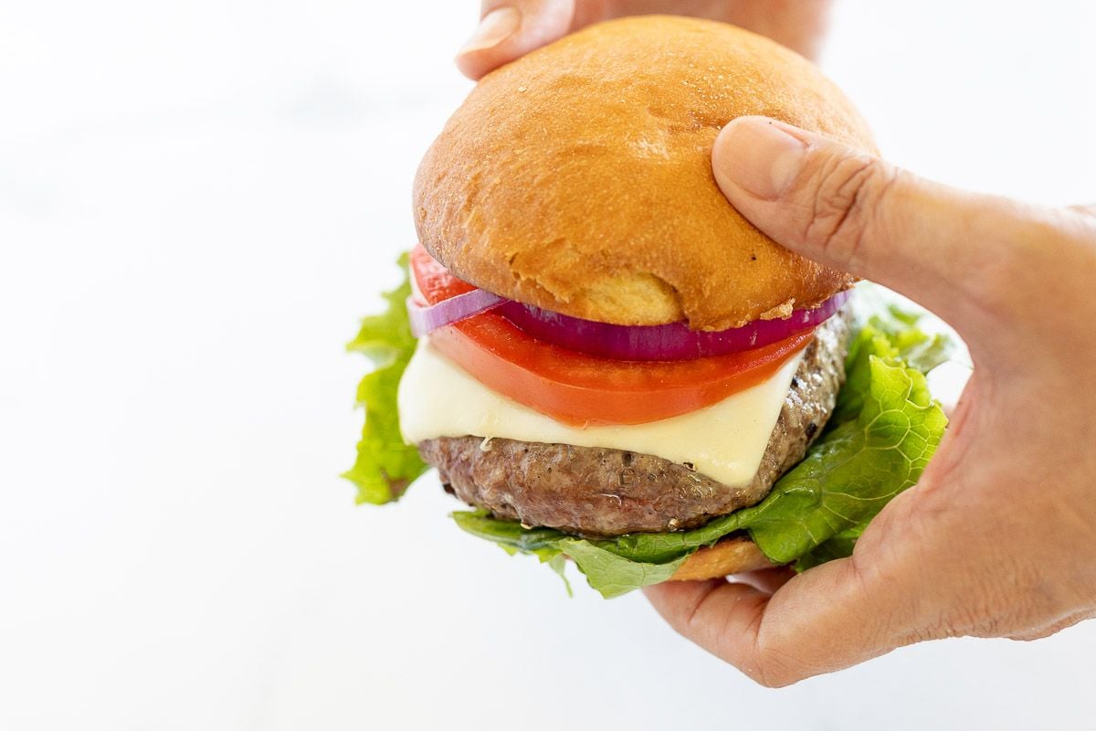 hands holding A hamburger stacked with lettuce, tomato, cheese and red onion.