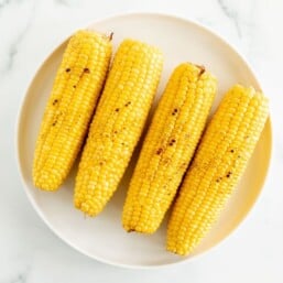 A white plate full of grilled sweet corn on a marble surface.