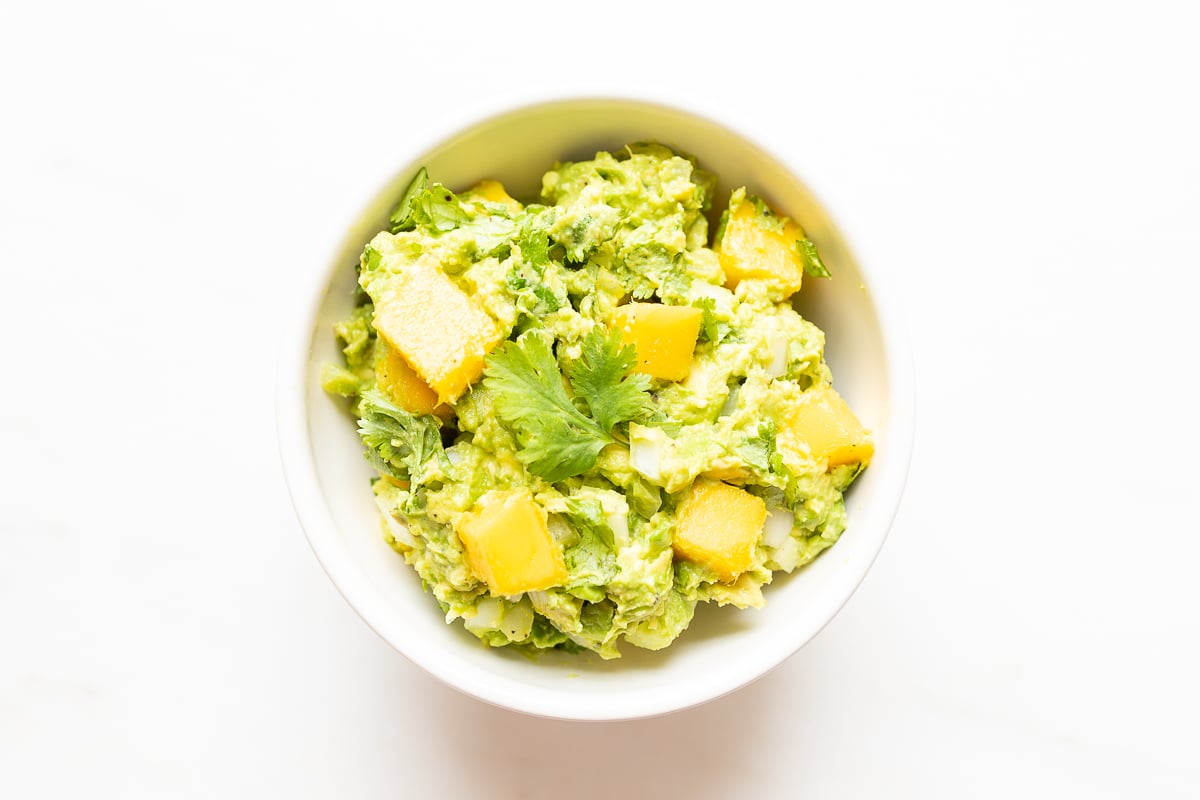 A white bowl of mango guacamole on a white countertop.