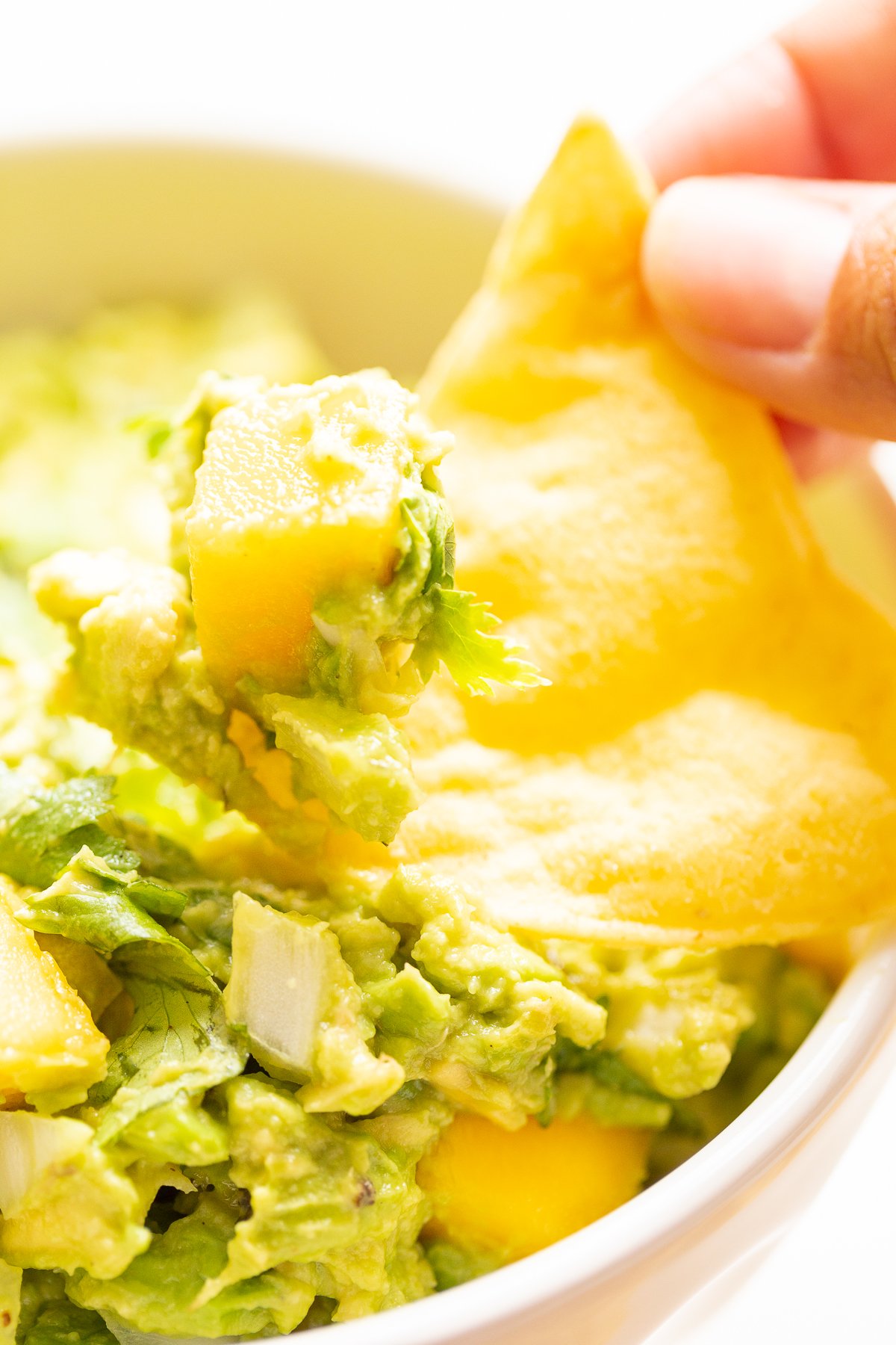 A hand dipping a tortilla chip into a bowl of mango guacamole.