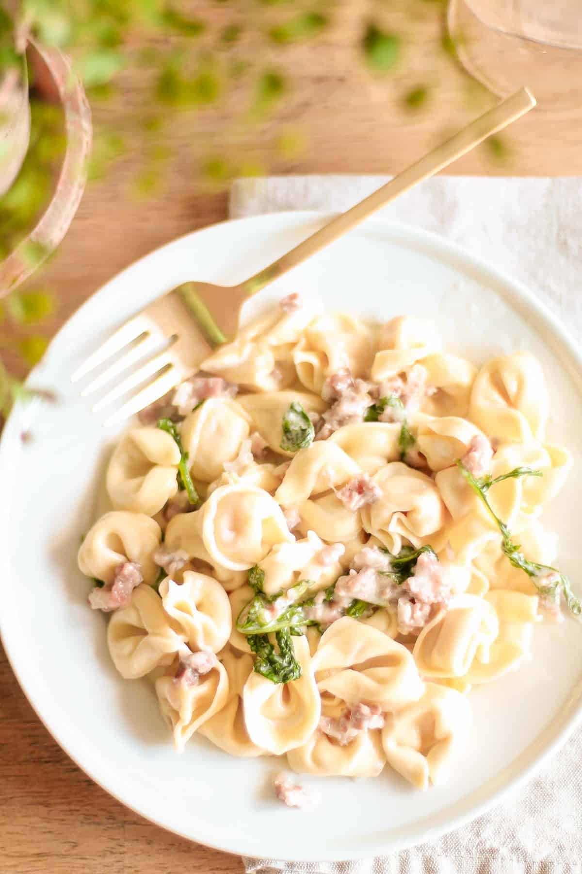 tortellacci with prosciutto arugula and truffle oil on white plate with gold fork