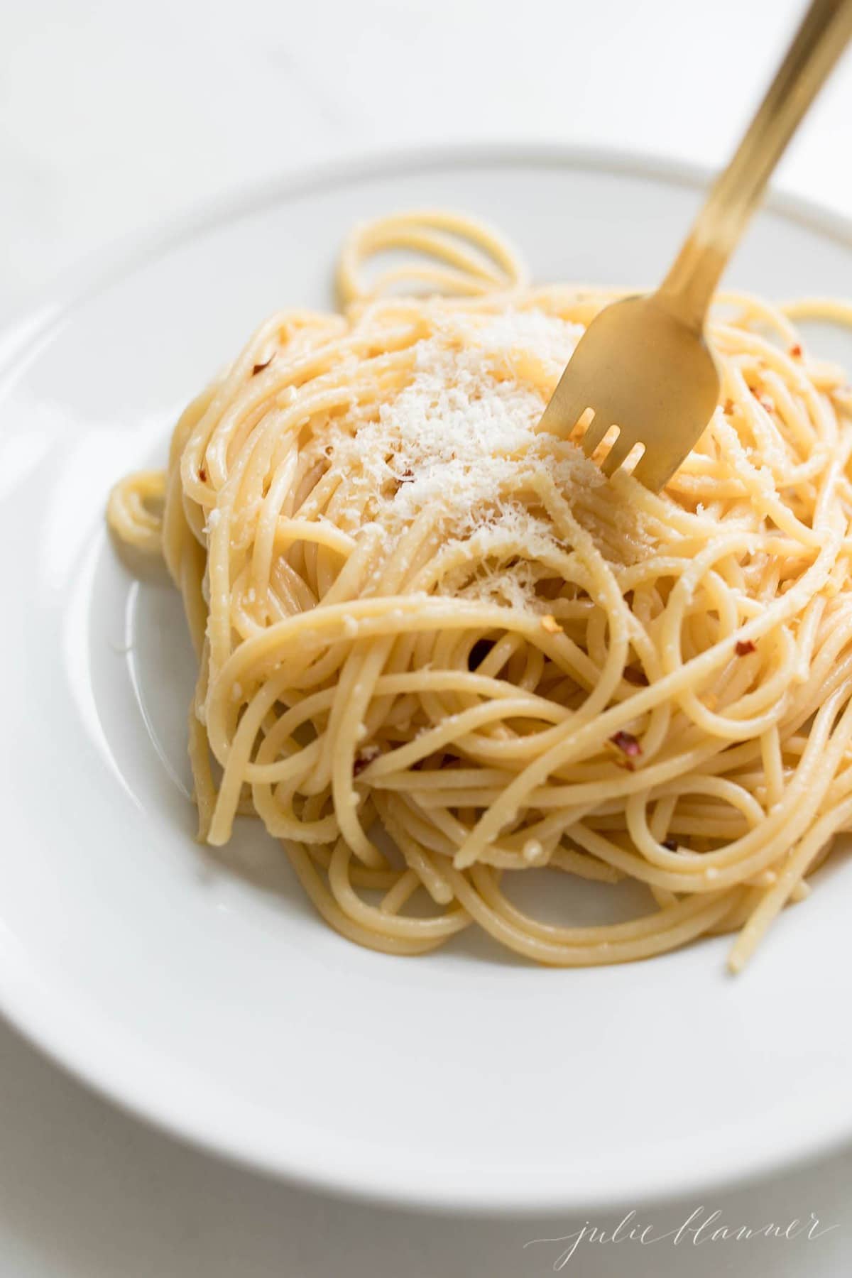 close up of pasta with red pepper flakes and gold fork twirling it