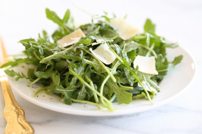 An arugula salad on a white plate, gold fork to the side.