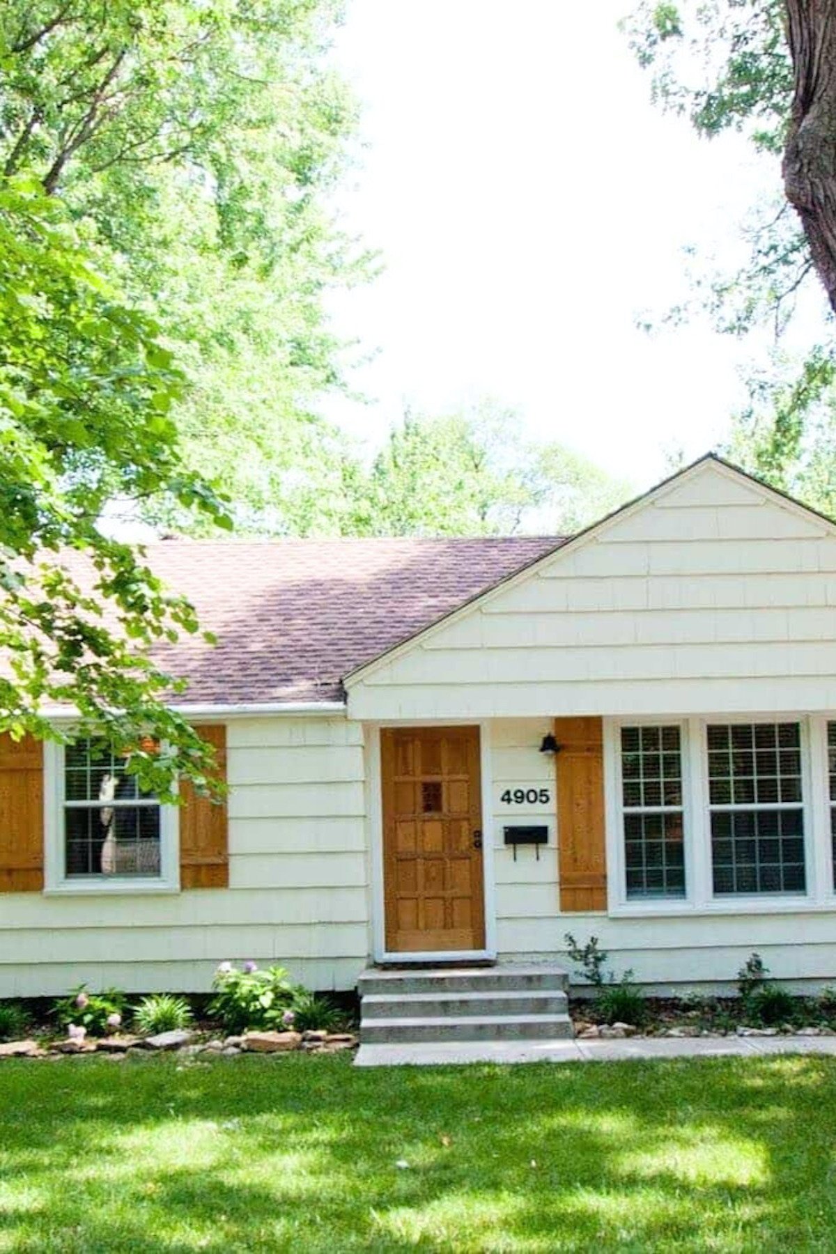 A shingled white cottage with a wood door, in a tutorial for how to remove paint from a wood door.