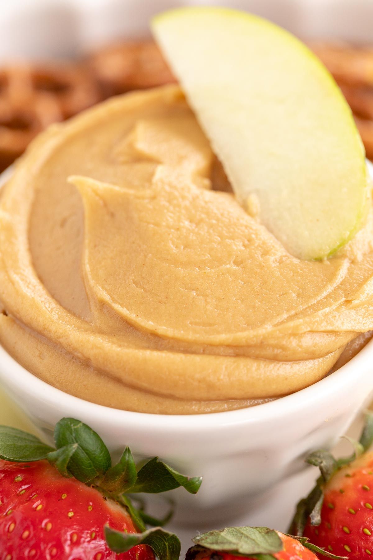 A white bowl full of peanut butter fruit dip, apple slice on top