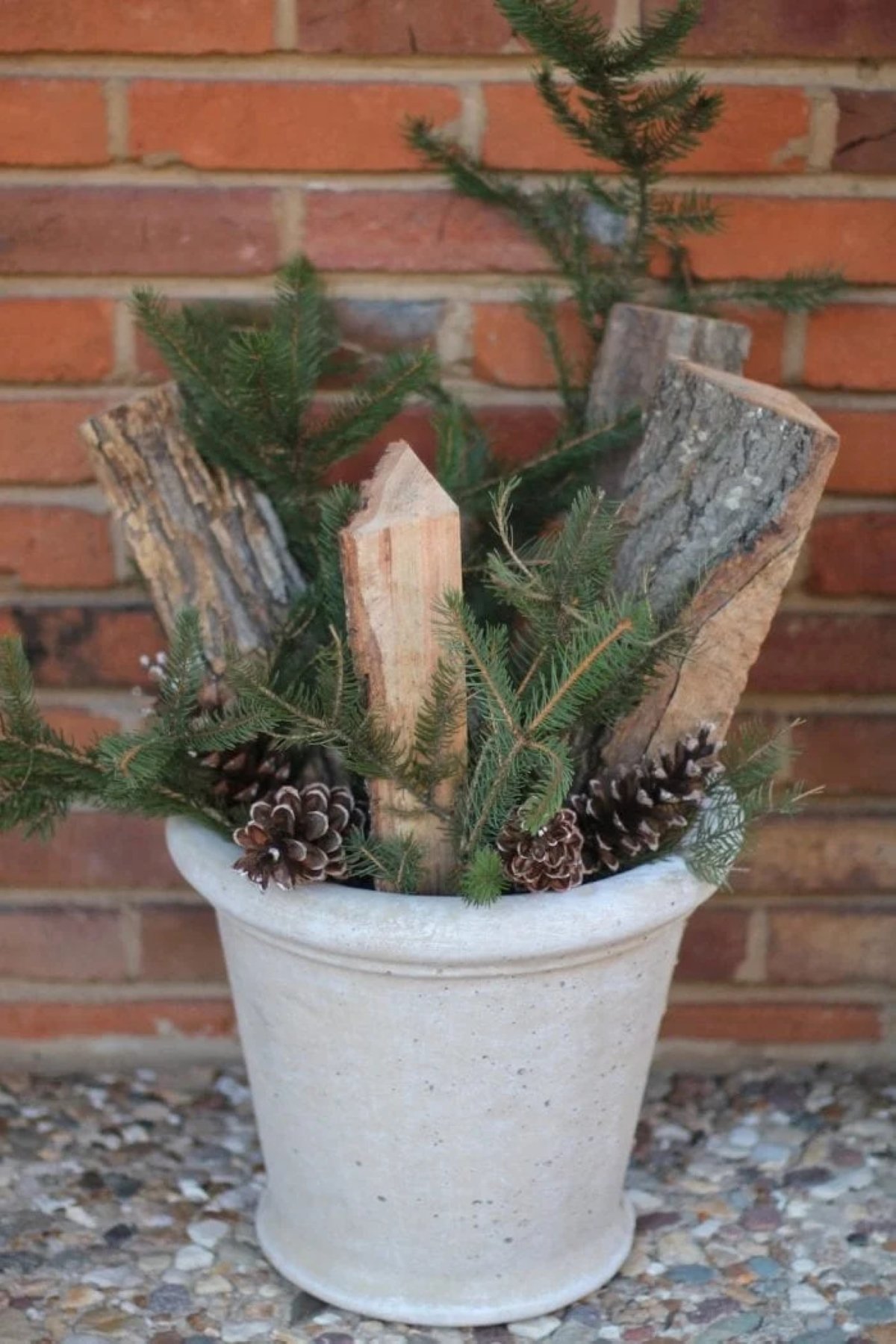 A winter planter for front porch with cut firewood, evergreens, pine cones