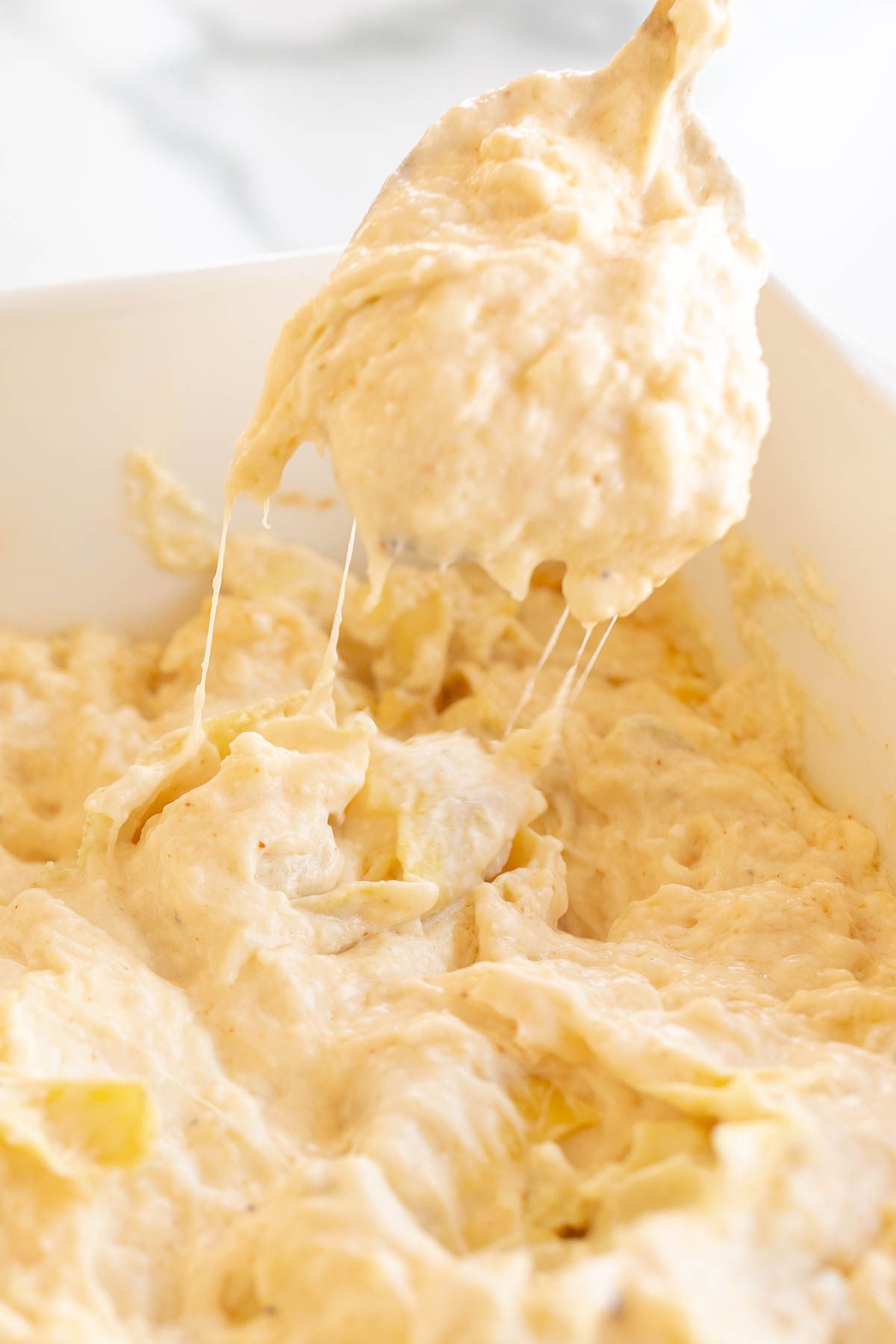 A white bowl full of a artichoke dip recipe, spoon scooping some out.