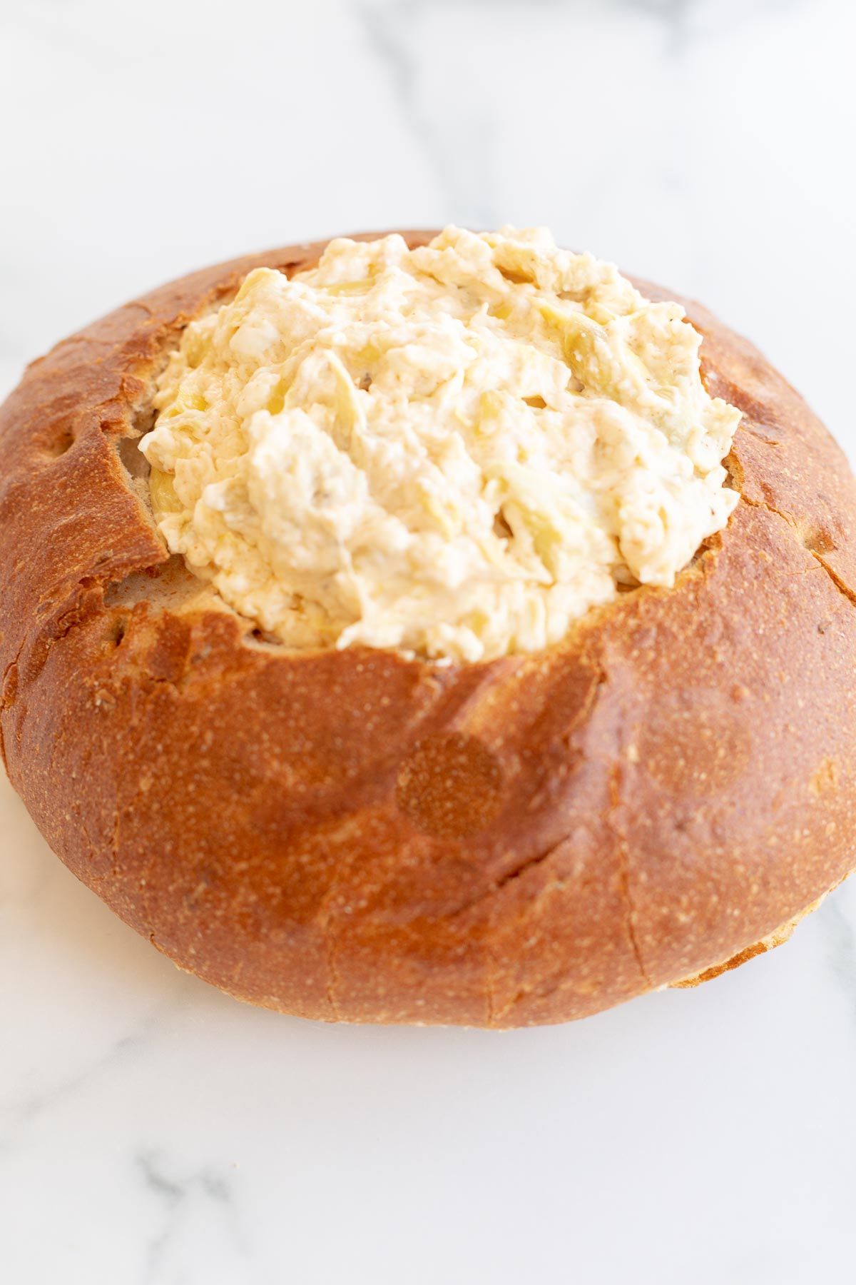 A bread bowl filled with artichoke dip