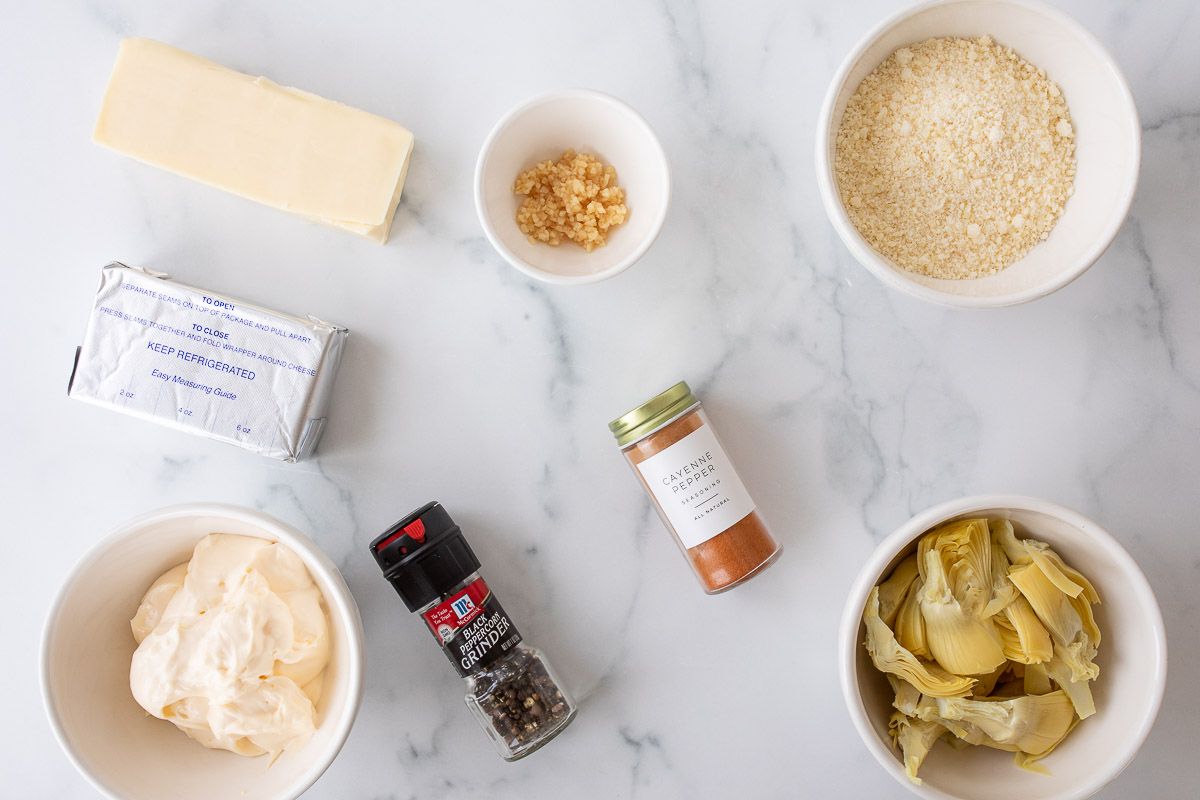 Ingredients for artichoke dip recipe laid out on a white marble surface