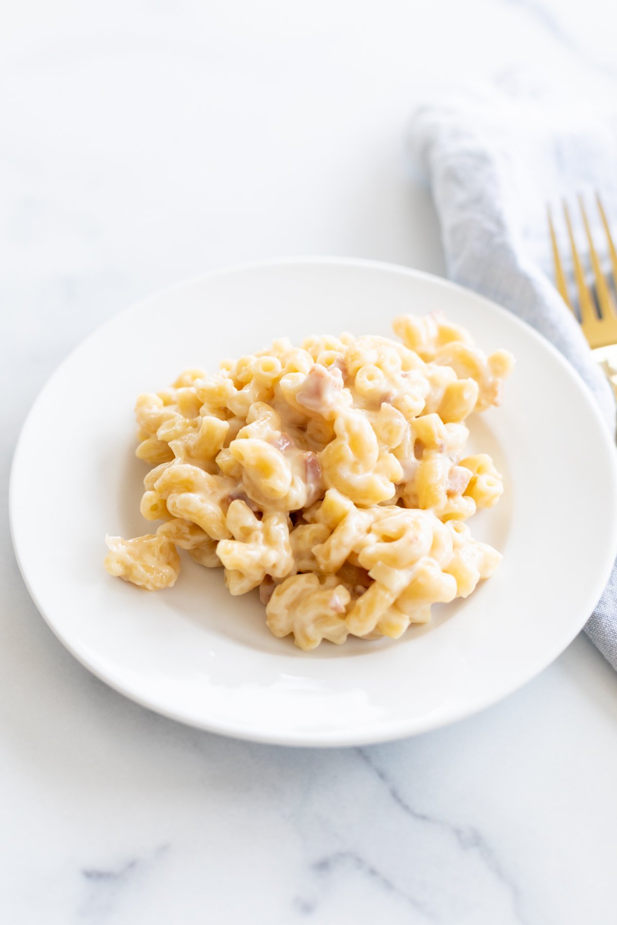 Gouda mac and cheese on a white plate with a gold fork to the side.