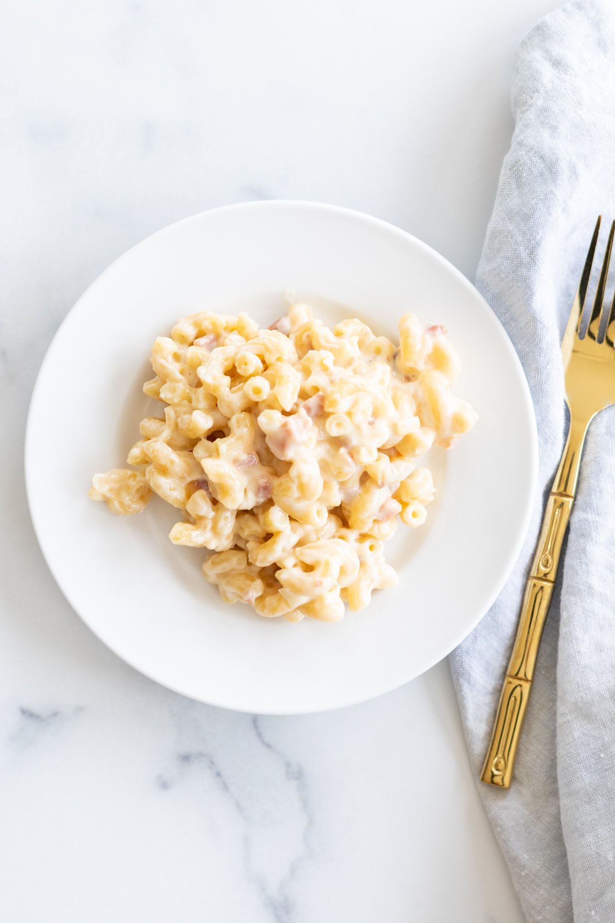 Gouda mac and cheese on a white plate with a gold fork to the side.