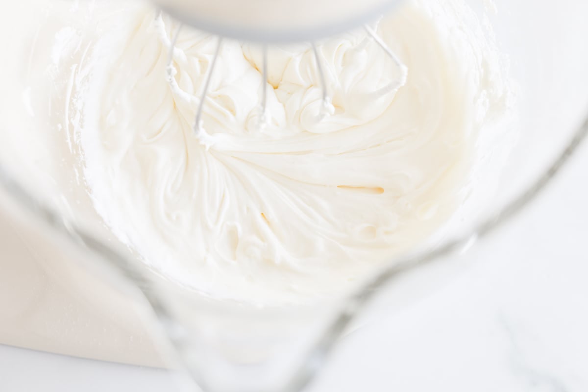 Sweet whipped cream in a bowl with a whisk.