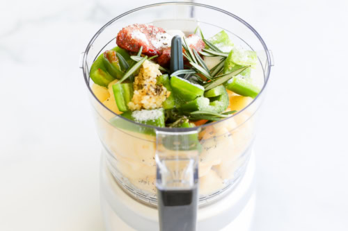 Ingredients including bell peppers, garlic, and herbs in a food processor, ready to be blended for chipotle vinaigrette.