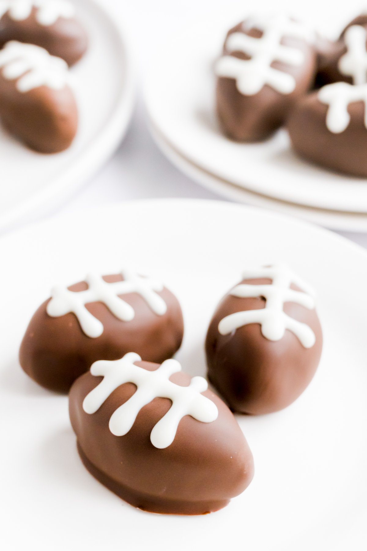 Peanut butter truffles shaped like footballs on plates decorated with white icing.