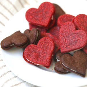 Homemade heart-shaped cookies resembling oreos are beautifully arranged on a plate.