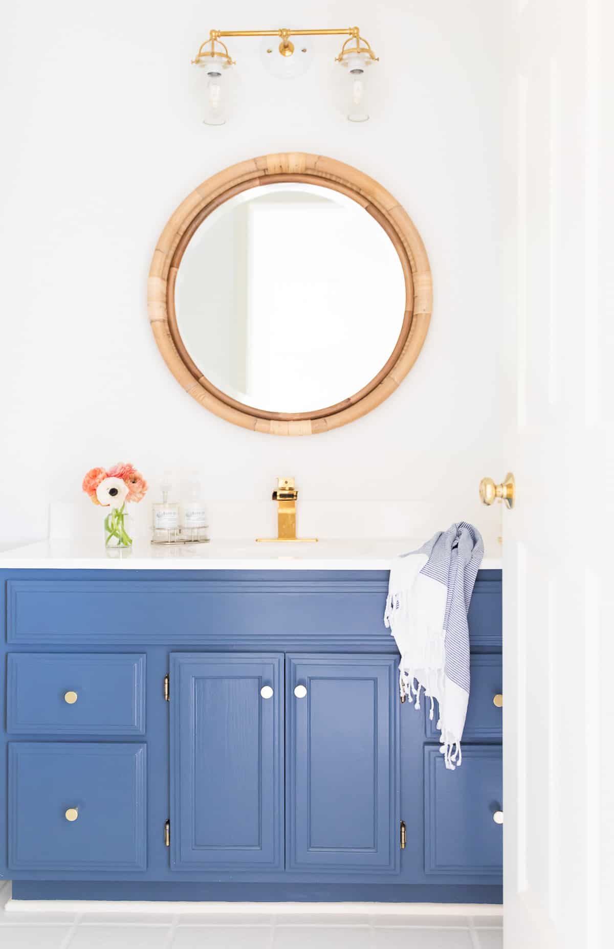 white and brass light over rattan mirror and blue vanity