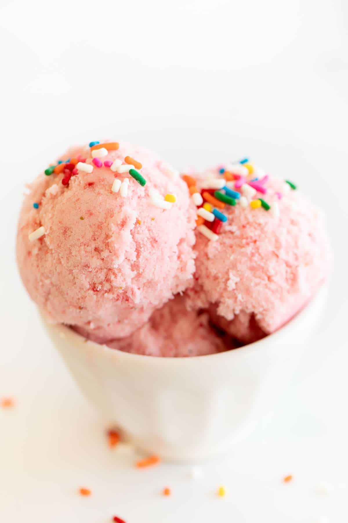 A white bowl of strawberry snow ice cream topped with rainbow sprinkles.